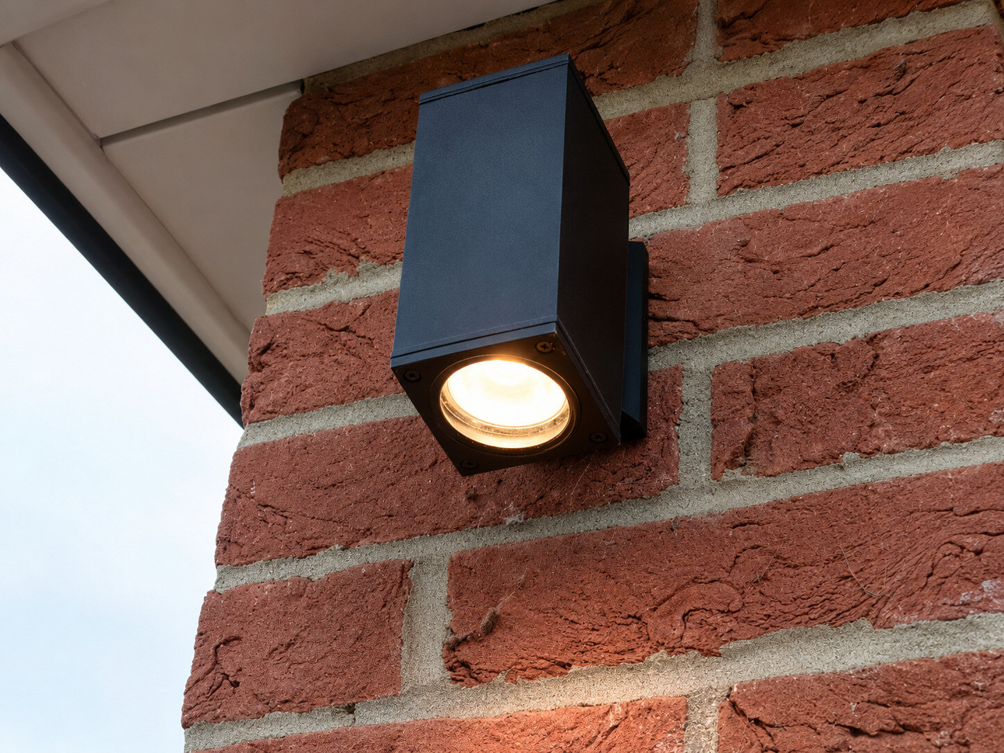 New black outdoor wall light illuminated on the brick wall of a garage